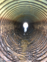 View down the inside of a corrugated metal pipe rusted through on the bottom